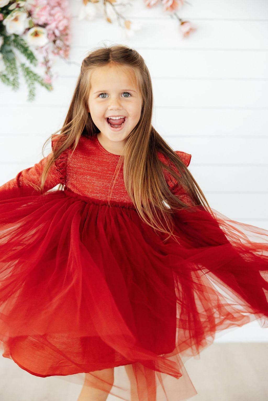 Young girl wearing red shimmer pumpkin spice tutu dress for girls twirling indoors with flowers in background