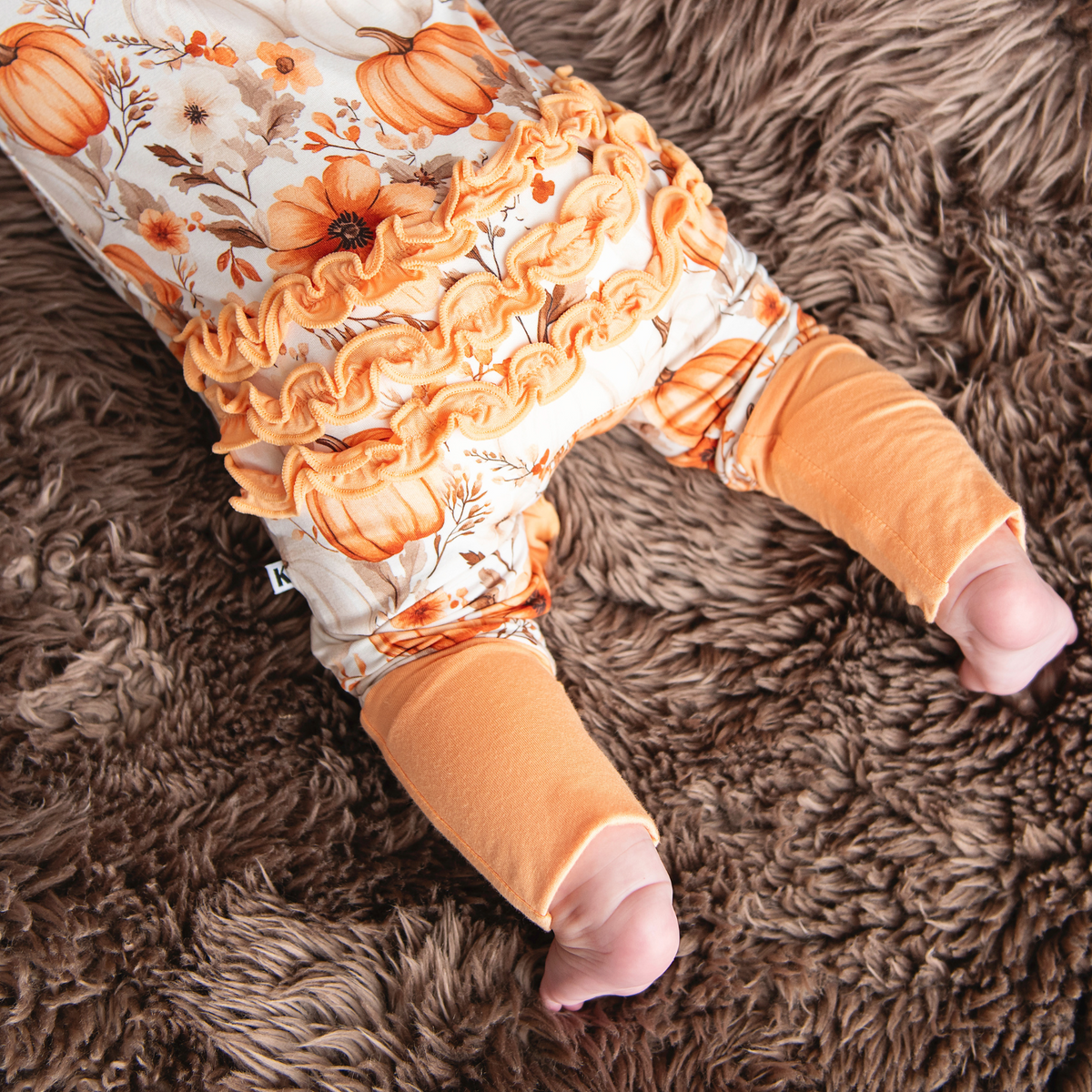 Baby legs in pumpkin-themed leggings on a brown fluffy surface