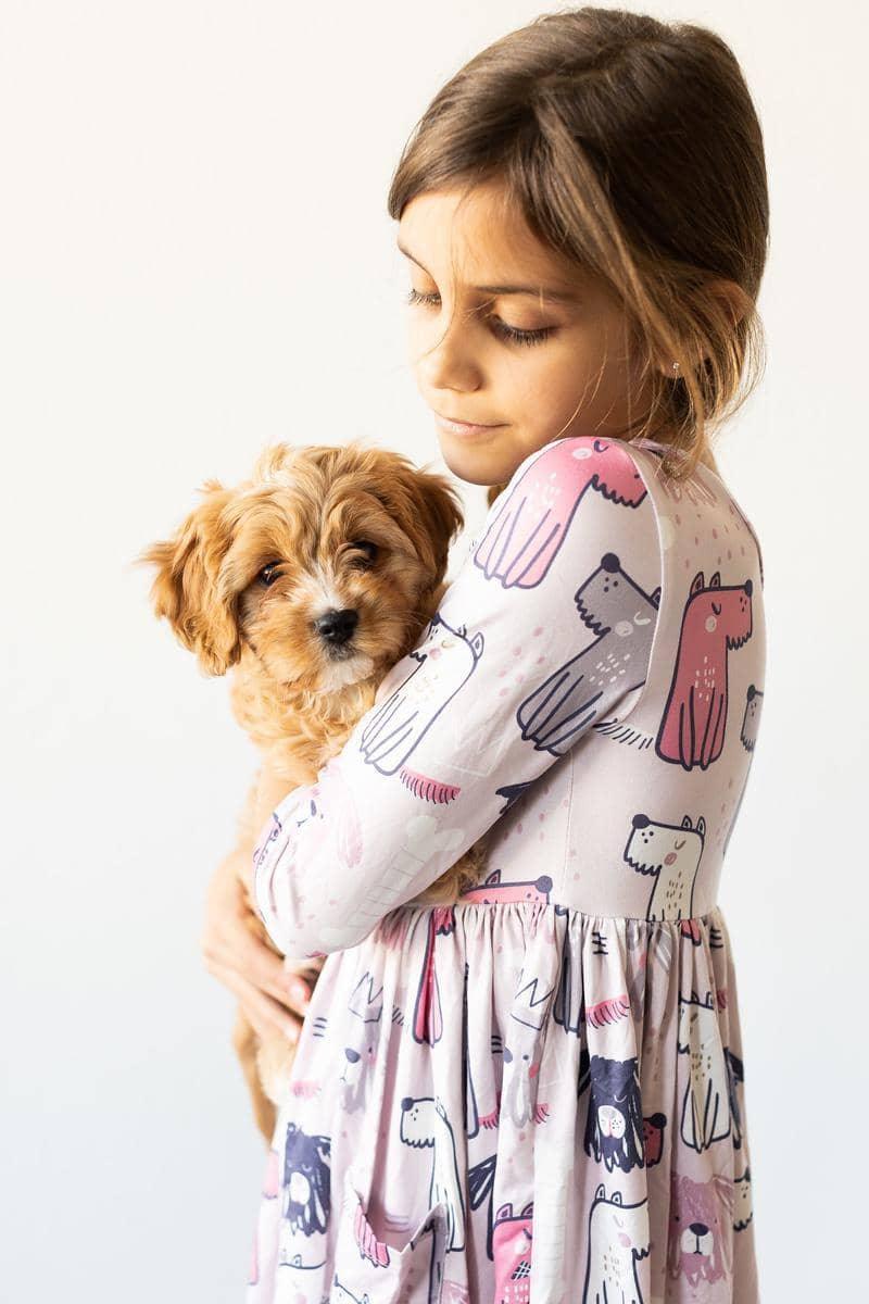 Girl wearing Mila & Rose puppy party dress for girls holding a small brown puppy while looking down