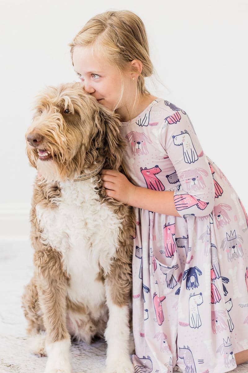 young girl wearing pink puppy party dress for girls twirl pocket dress  hugging a large brown and white dog