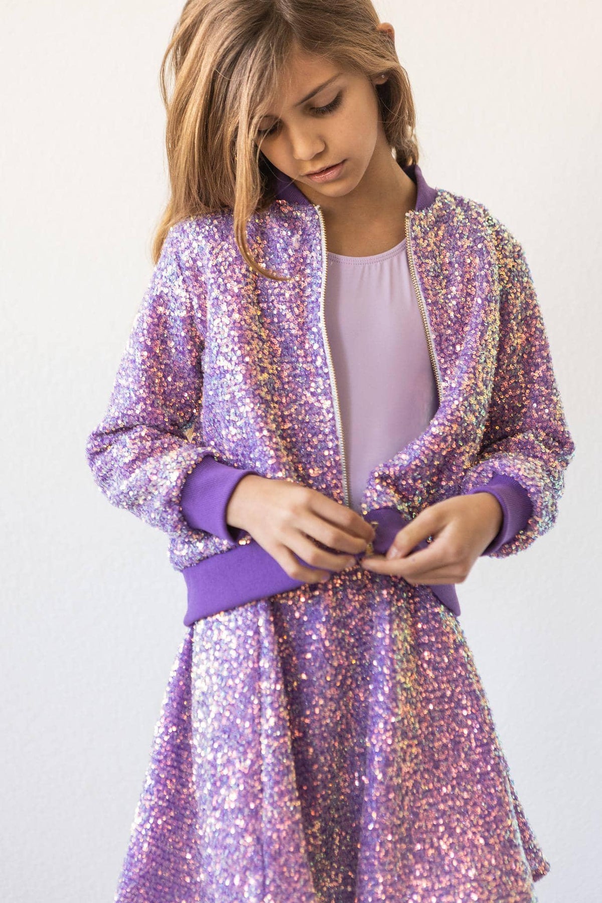 girl wearing purple sequin jacket for kids and matching skirt while buttoning the jacket