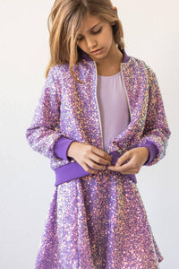 girl wearing purple sequin jacket for kids and matching skirt while buttoning the jacket