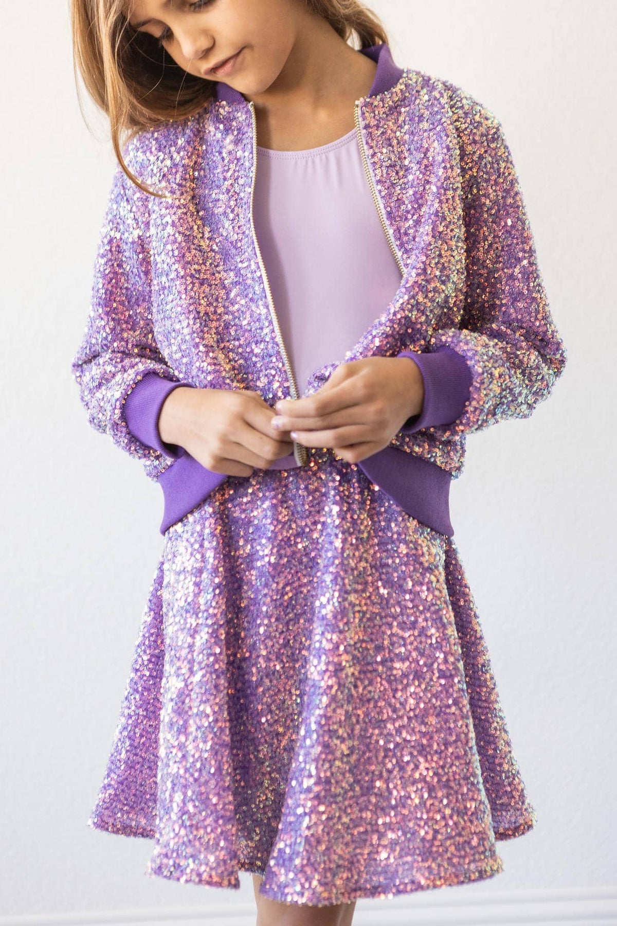 girl wearing purple sequin jacket for kids with matching skirt buttoning jacket
