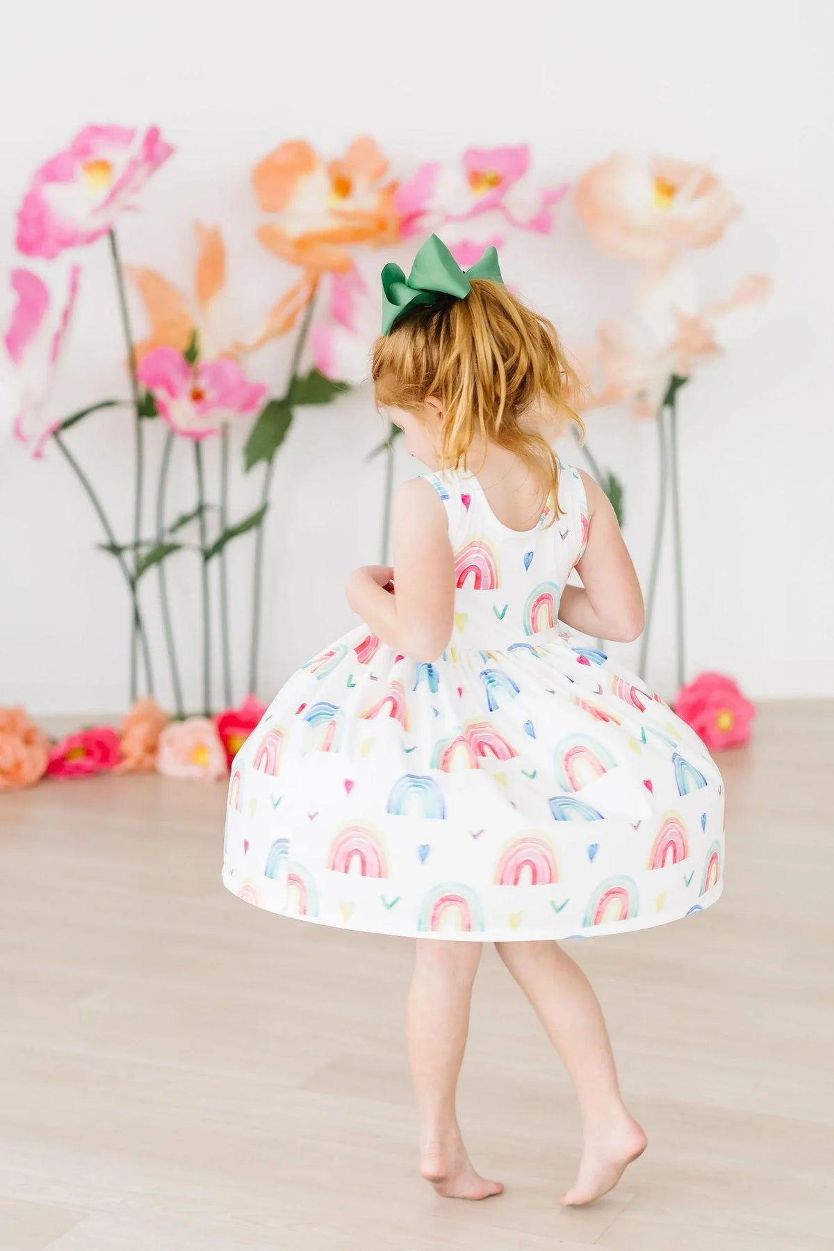 young girl twirling in white rainbow tank twirl dress for girls with colorful rainbows and green bow in hair