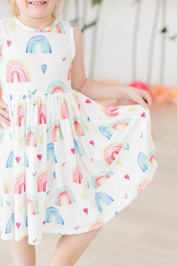 Little girl wearing rainbow tank twirl dress for girls holding the skirt and smiling