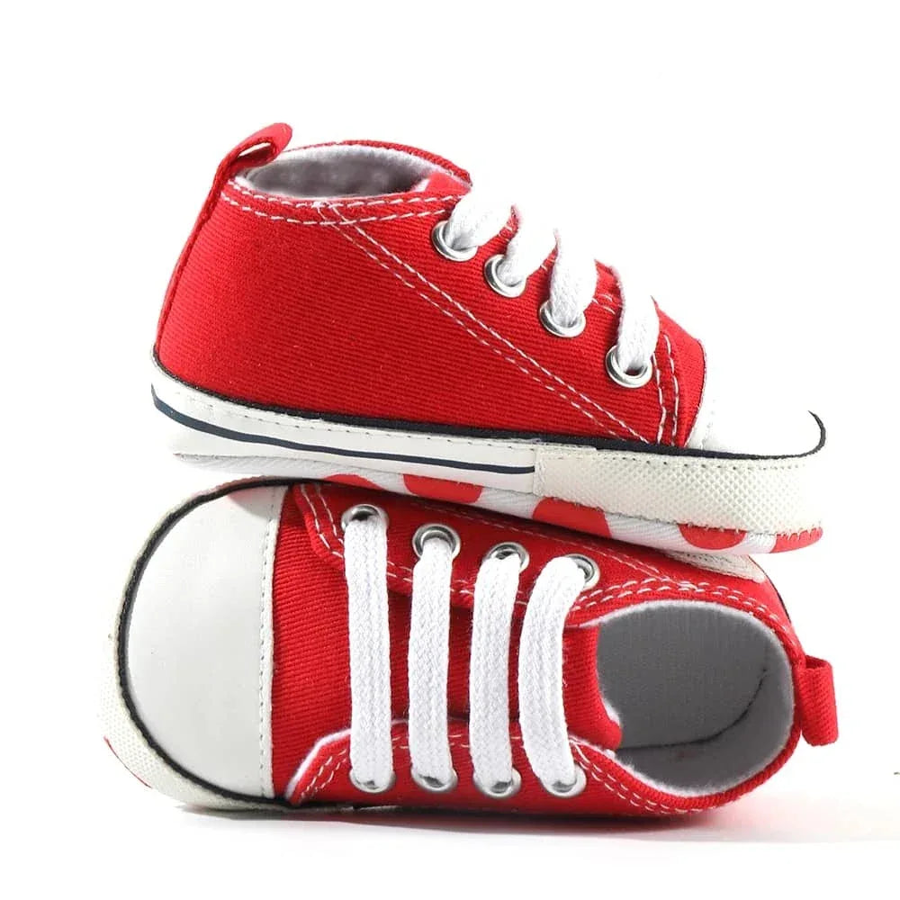 Pair of red canvas baby shoes for infants with white laces and rubber soles shown from side and top views