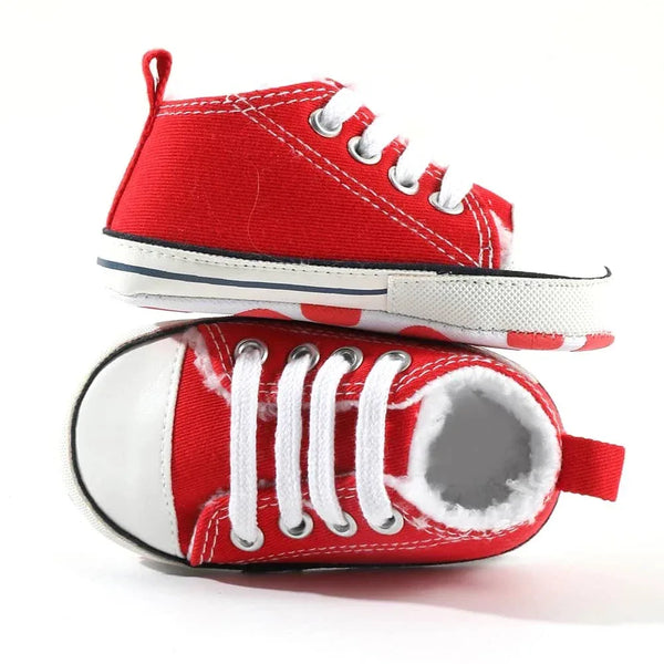 Pair of red canvas baby shoes for infants with white laces and soft sole, one shoe lying flat and the other standing upright