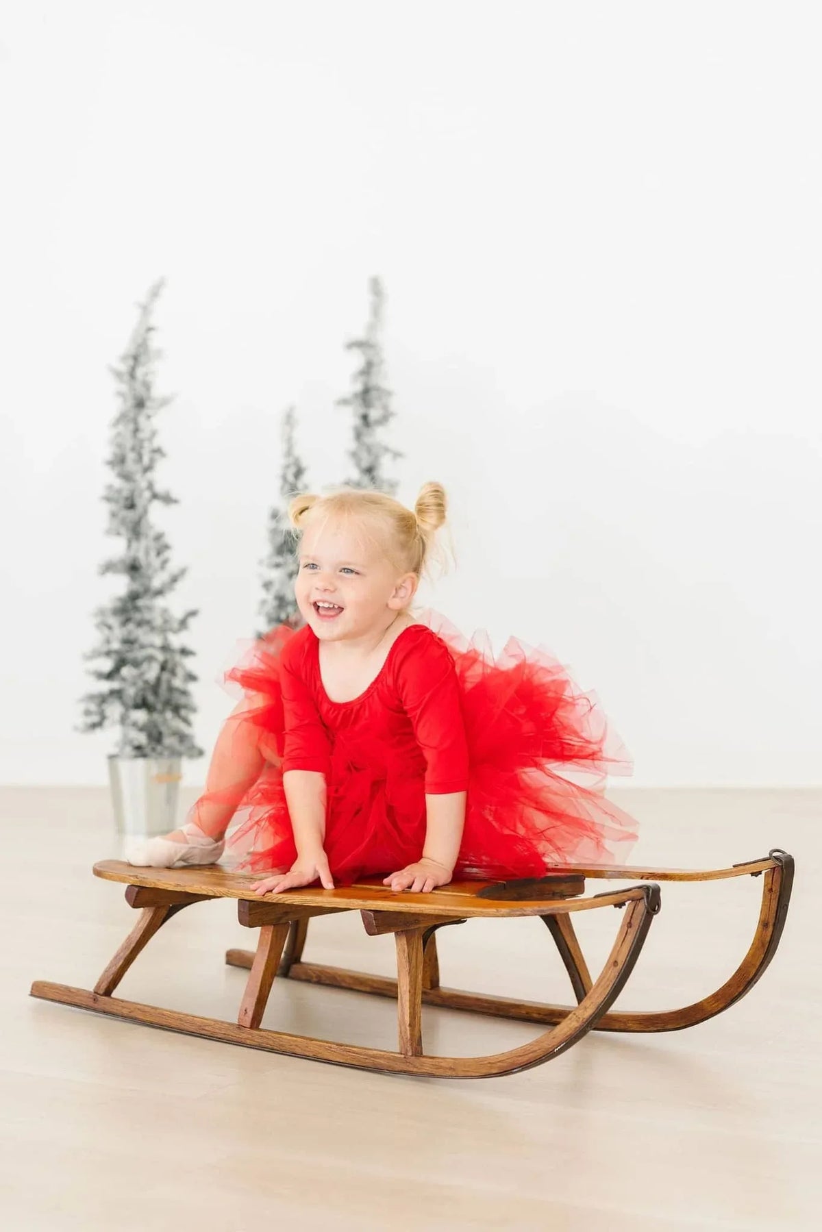 Toddler girl wearing red holiday tutu leotard for girls with 3/4 sleeves sitting on wooden sled