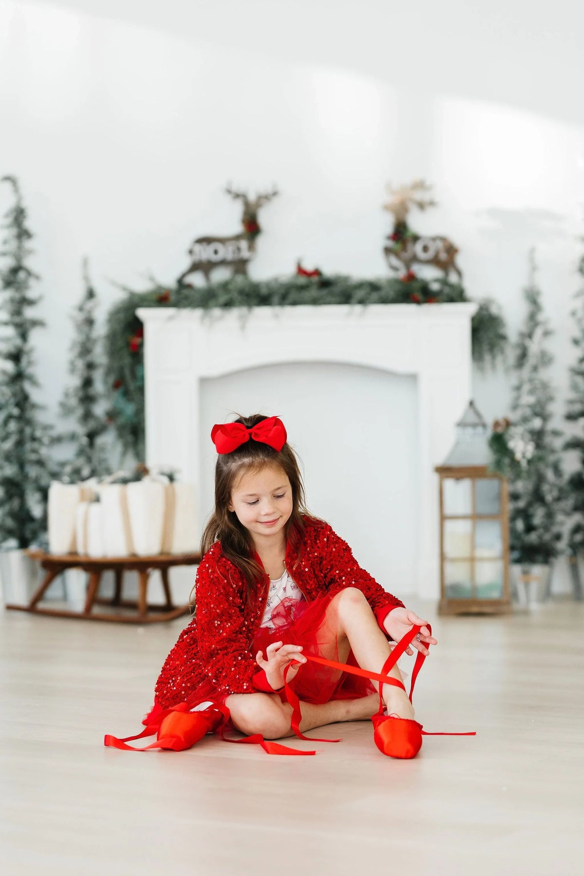 Red sequin jacket for girls, long sleeve, worn by young girl sitting indoors tying red ballet shoes