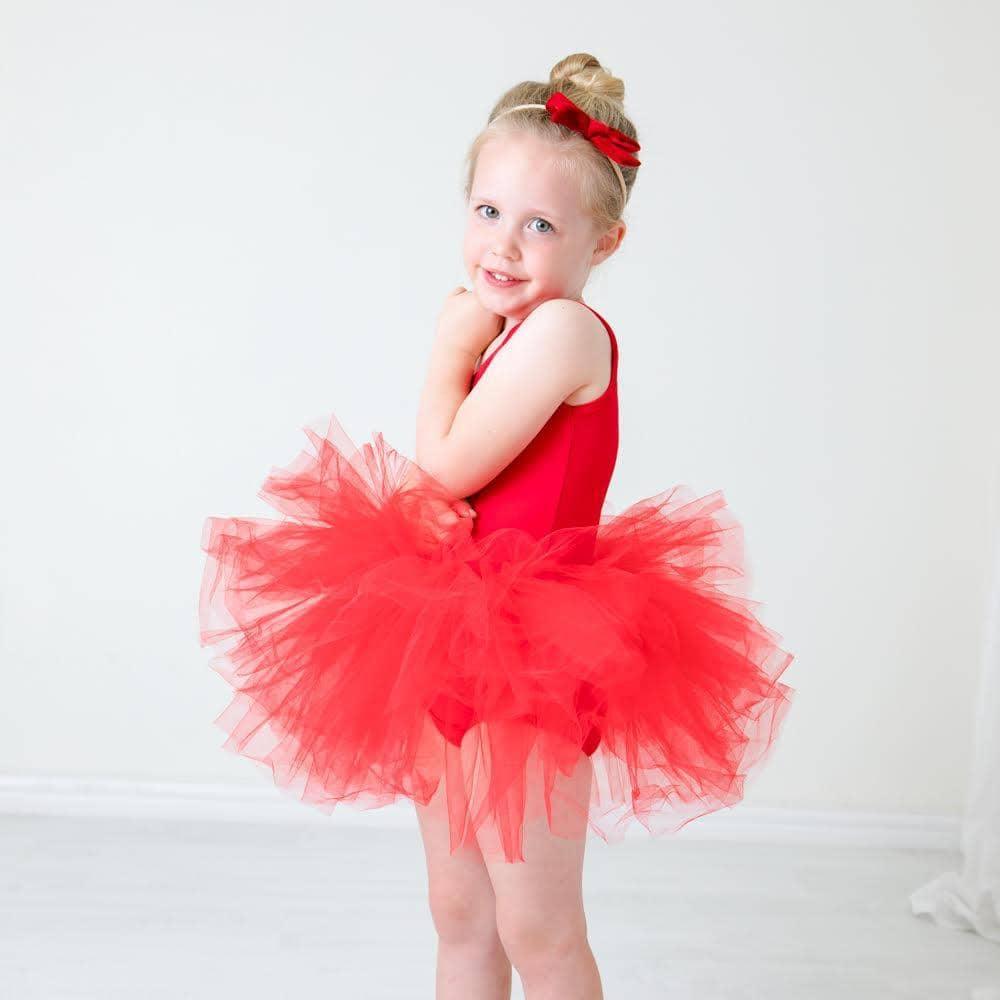 Young girl wearing red tutu leotard smiling and posing with hands near face
