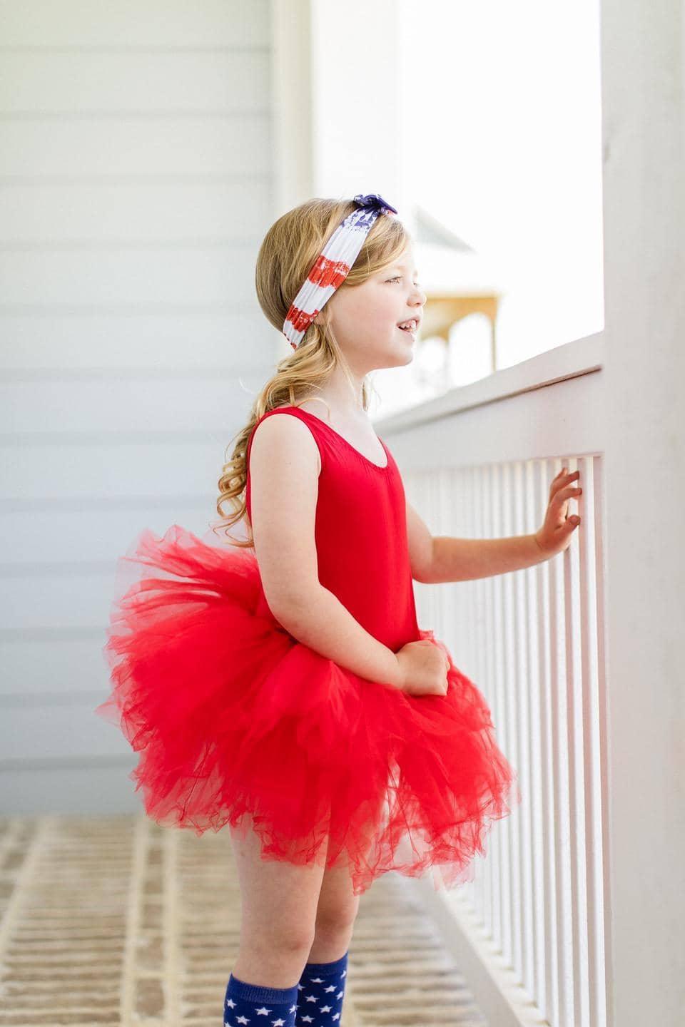 young girl wearing red tutu leotard standing and looking outside on porch railing