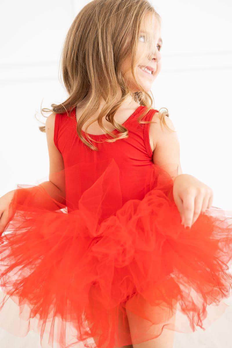 Young girl wearing red tutu leotard smiling and twirling in bright light