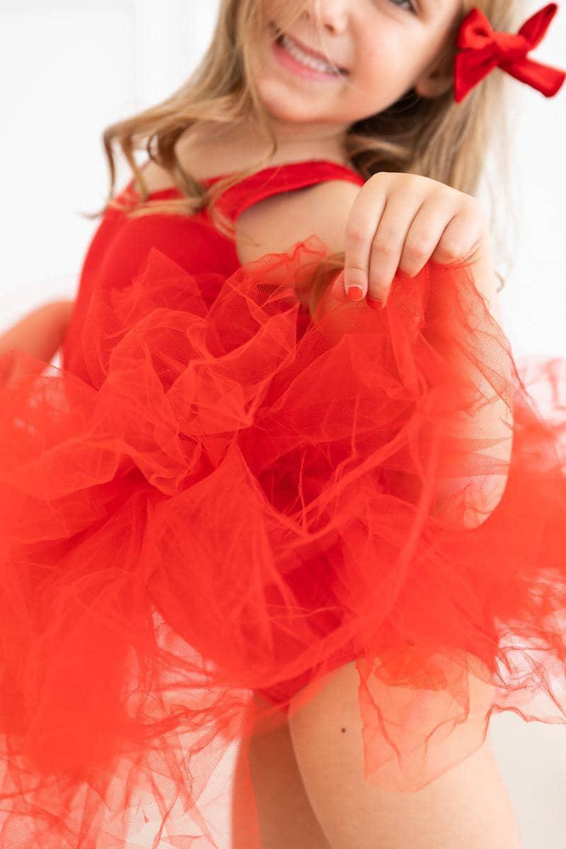 young girl wearing red tutu leotard holding up skirt smiling with red bow in hair