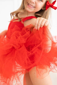 young girl wearing red tutu leotard holding up skirt smiling with red bow in hair