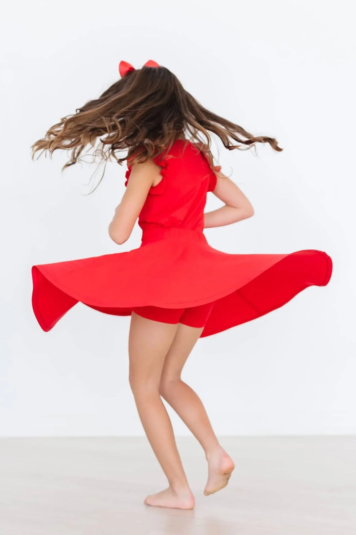 young girl wearing red twirl skort for girls spinning with flowing skirt and bow in hair