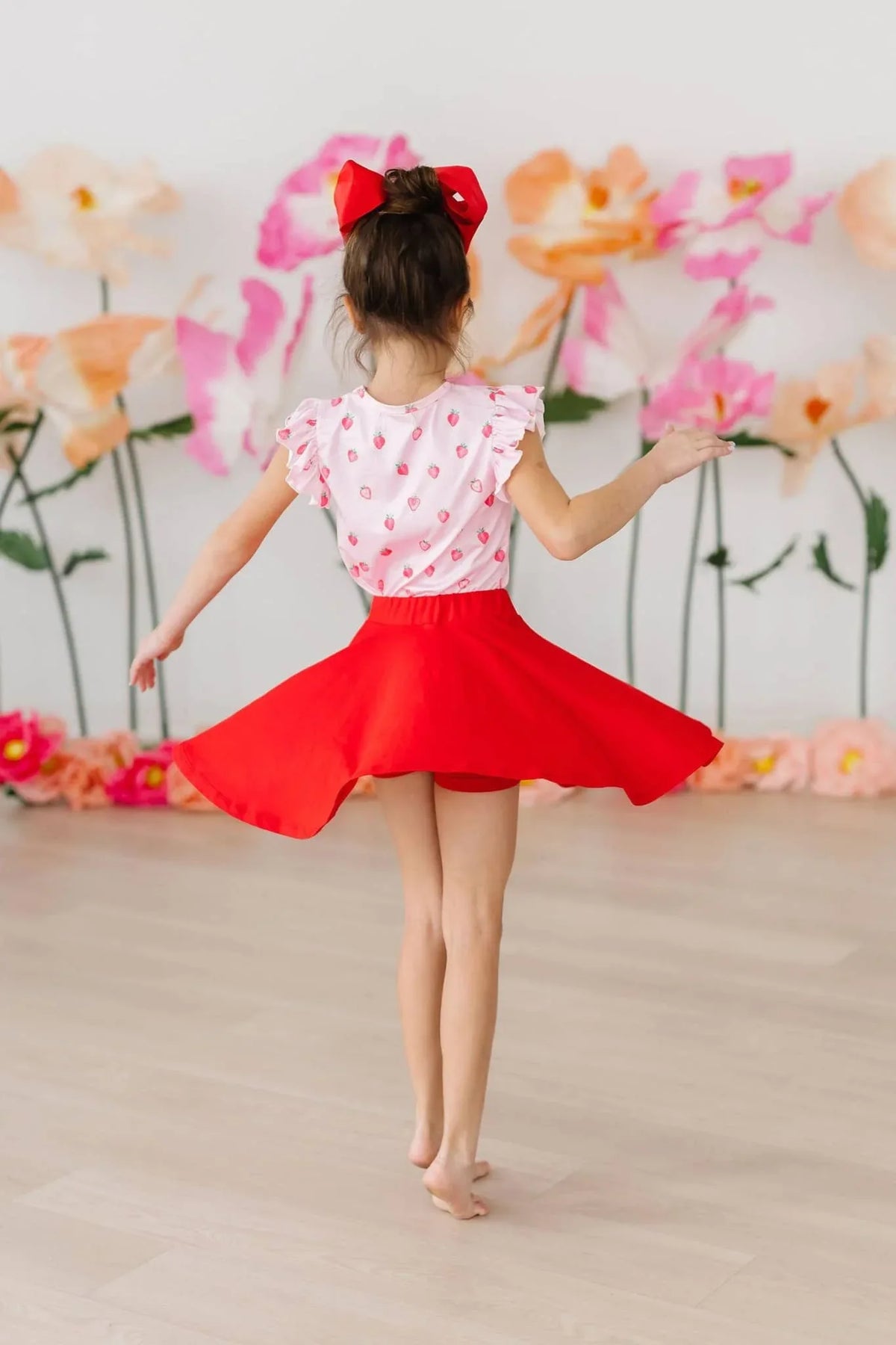 girl twirling in red twirl skort for girls with red bow in hair and floral background