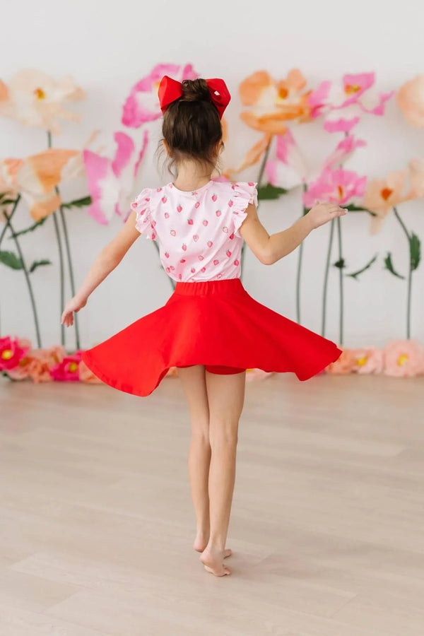 girl twirling in red twirl skort for girls with red bow in hair and floral background