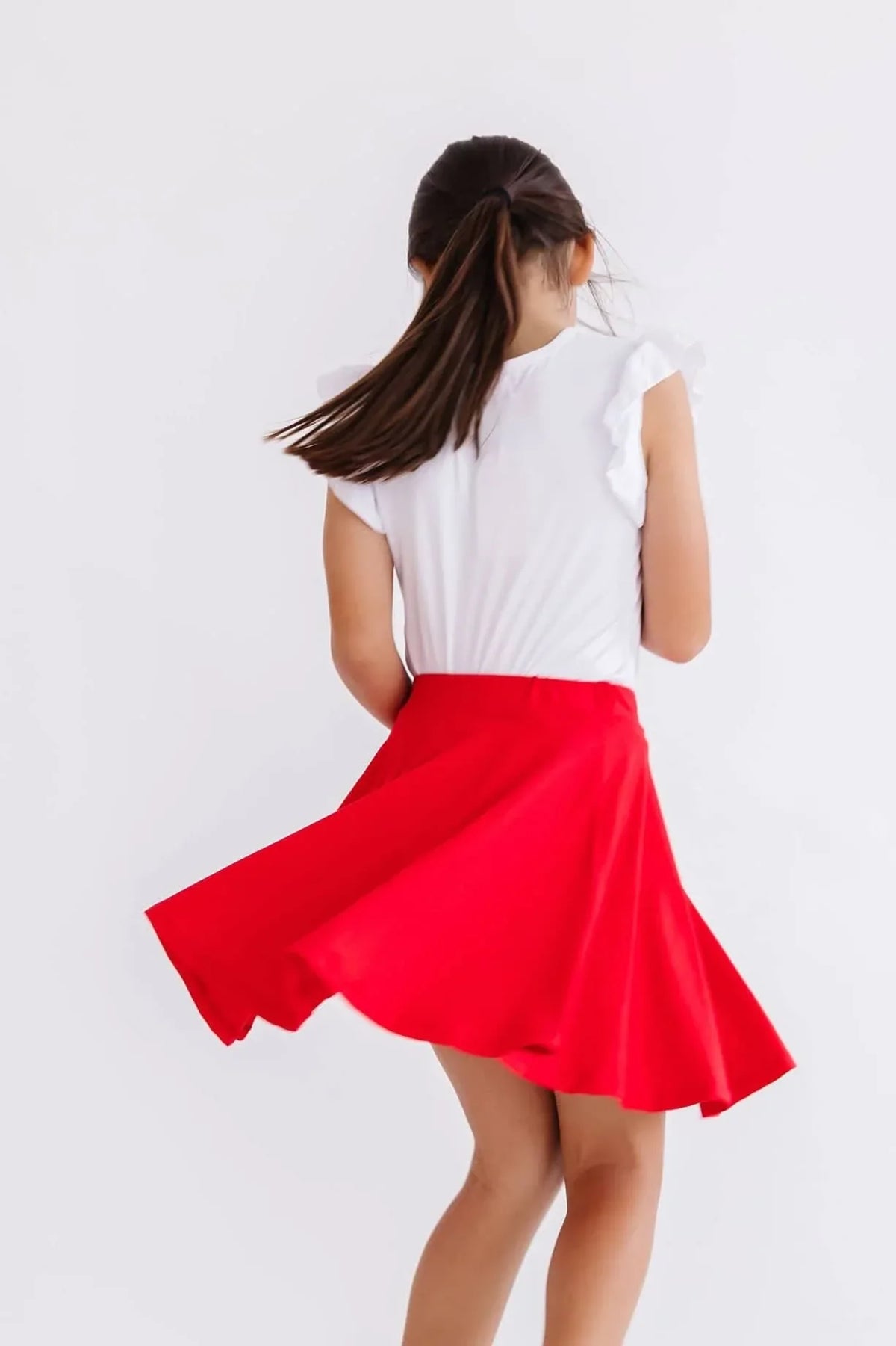 Girl wearing red twirl skort for girls spinning with white top against white background