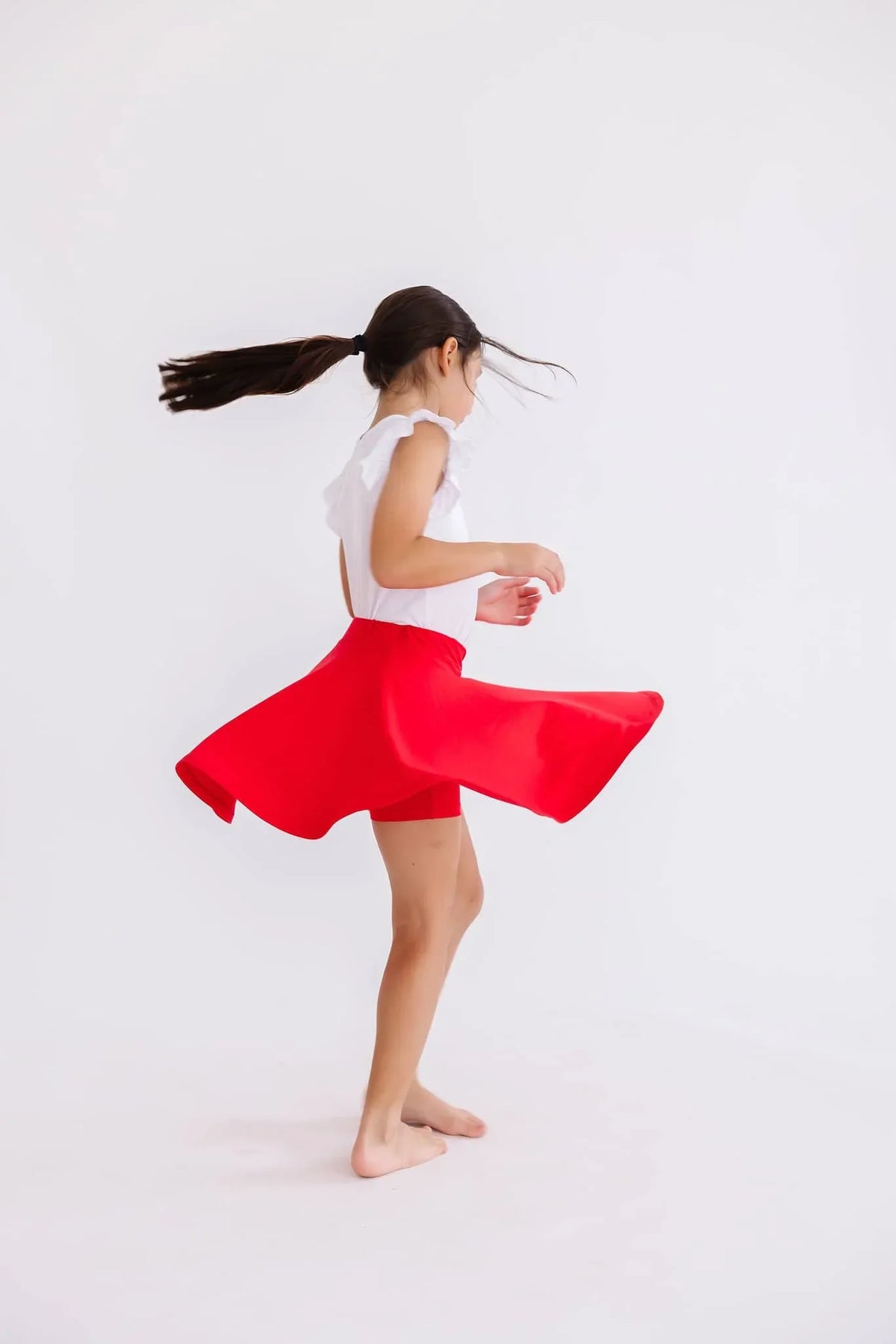 Girl wearing red twirl skort for girls spinning with ponytail in motion on white background