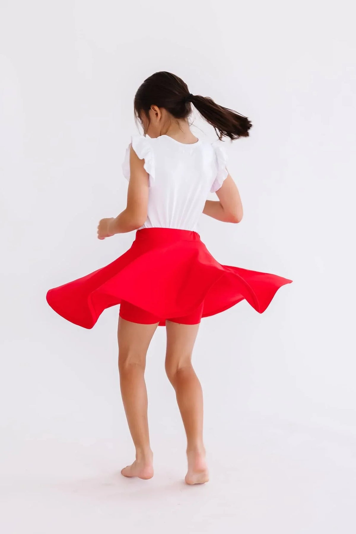 Young girl twirling in a red twirl skort for girls with a white flutter sleeve top