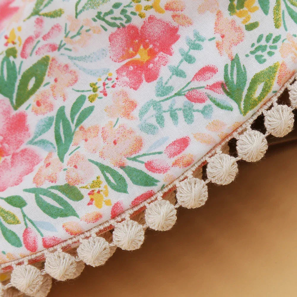Close-up of floral reversible baby bib and headband set with pink and green pattern and white pompom trim for infants