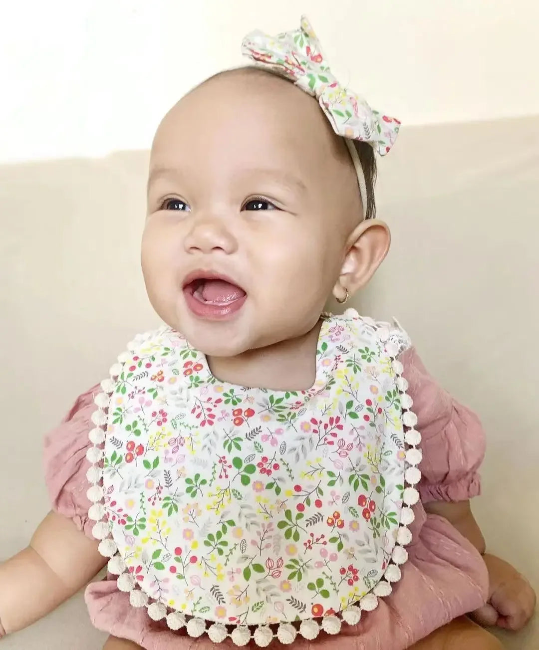 baby wearing floral reversible baby bib and headband set smiling and sitting in pink outfit