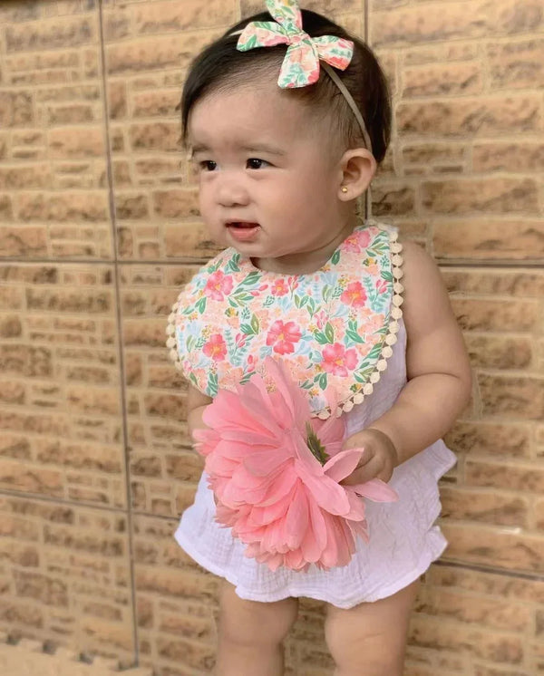 baby girl wearing reversible baby bib and headband set with floral pattern holding pink flower