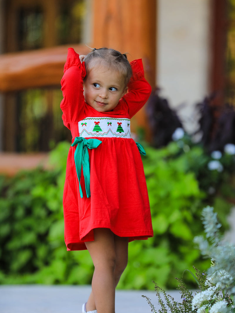 Toddler in red Christmas smocked dress with green bow and tree embroidery posing outdoors