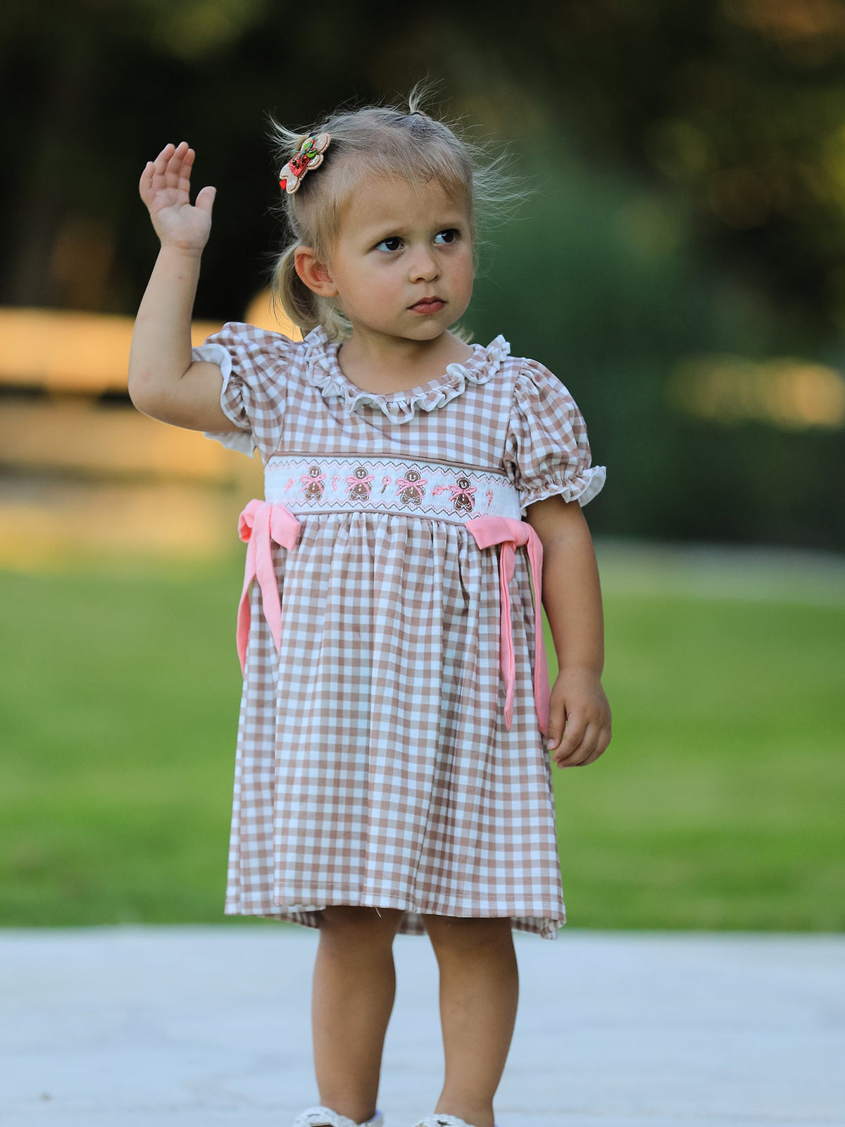 Child wearing vintage plaid dress with embroidered gingerbread, pink bows, and ruffled neckline.