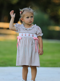 Child wearing vintage plaid dress with embroidered gingerbread, pink bows, and ruffled neckline.