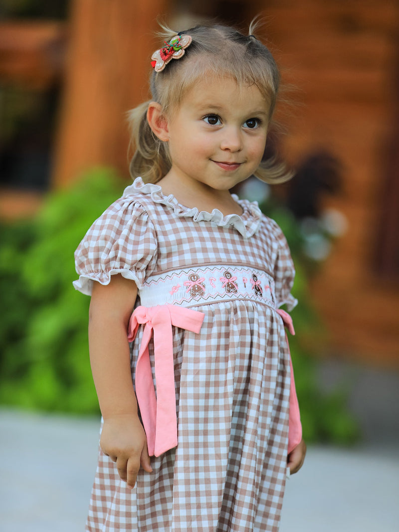 Little girl wearing Christmas vintage-style plaid dress with embroidered gingerbread and pink bows.