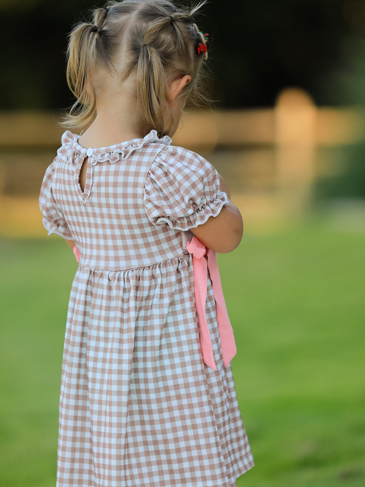 Back view of a vintage plaid dress with pink ribbons, ruffled sleeves, and a keyhole back on a toddler.