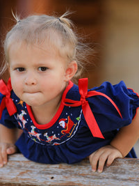 Toddler in navy Christmas dress with Santa sleigh embroidery and red bows on sleeves for holiday celebrations.