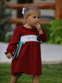 Red Christmas girls dress with festive smocking embroidery of a dog and holiday lights, accented by a green plaid bow.