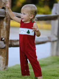 Toddler boy in red Christmas romper with smocked chest featuring embroidered tree, dog, and lights.
