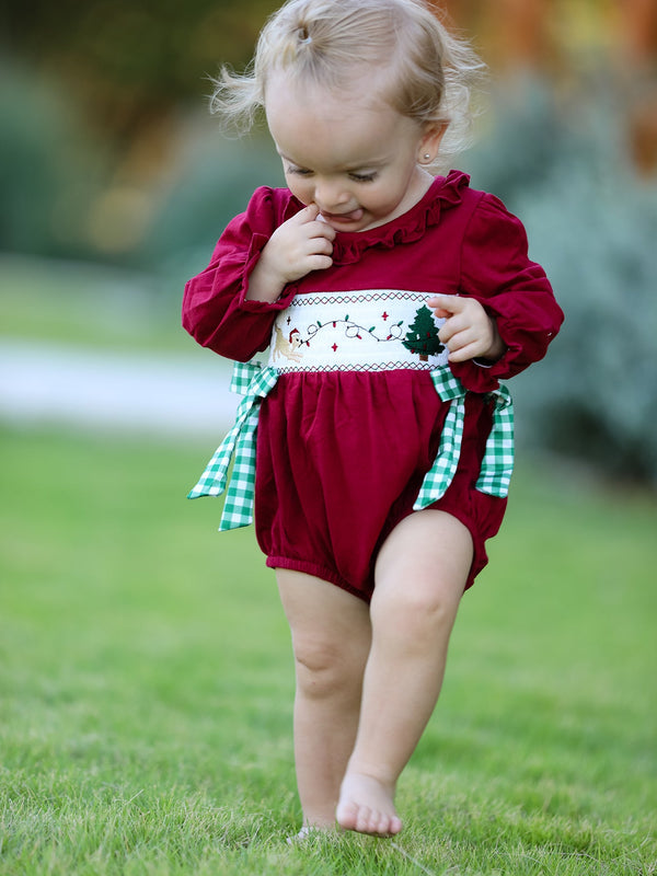 Baby girl in red Christmas romper with festive tree embroidery and green plaid side ties.