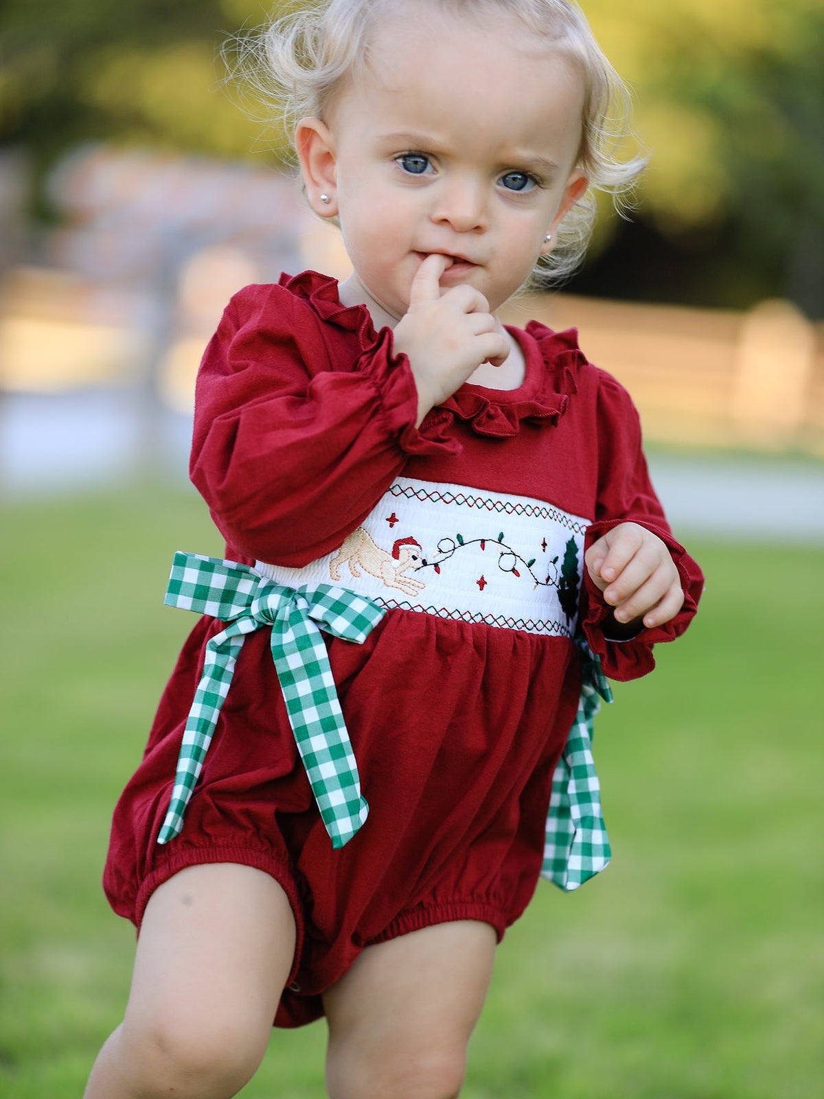 Red baby girls Christmas romper featuring festive reindeer embroidery and a green plaid bow sash.