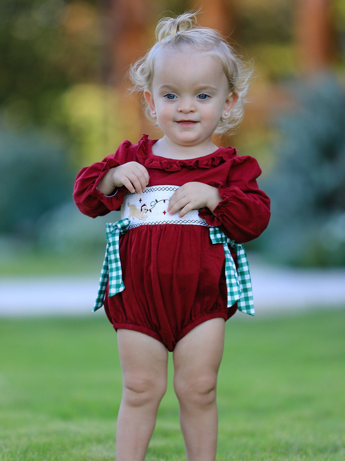 Baby girl wearing a red Christmas romper with festive embroidery and green plaid side bows.