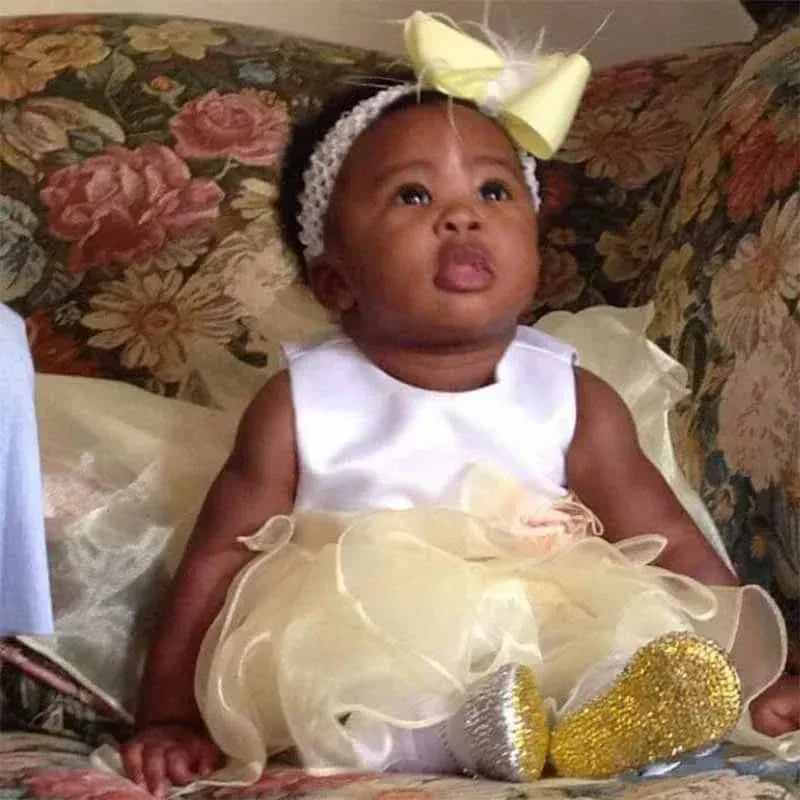 baby girl wearing yellow rhinestone first walker baby shoes sitting on floral couch