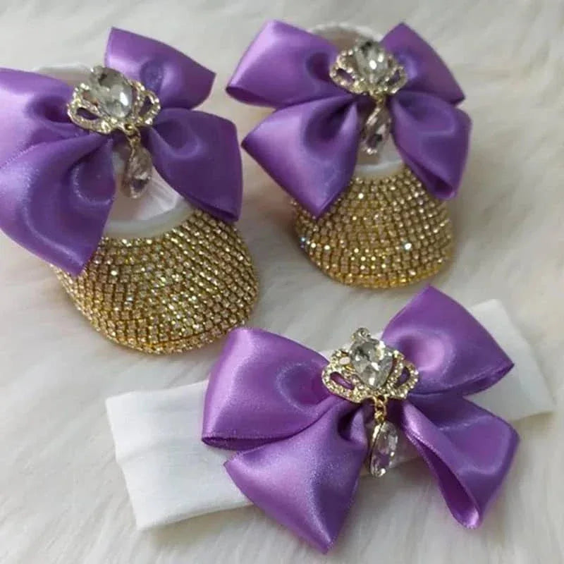 Baby wearing gold rhinestone first walker baby shoes with large purple bows and jeweled crowns