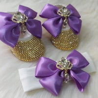 Baby wearing gold rhinestone first walker baby shoes with large purple bows and jeweled crowns