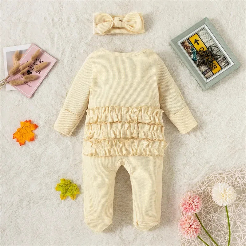 Cream ribbed knit baby romper with headbow for infants laid flat on white surface