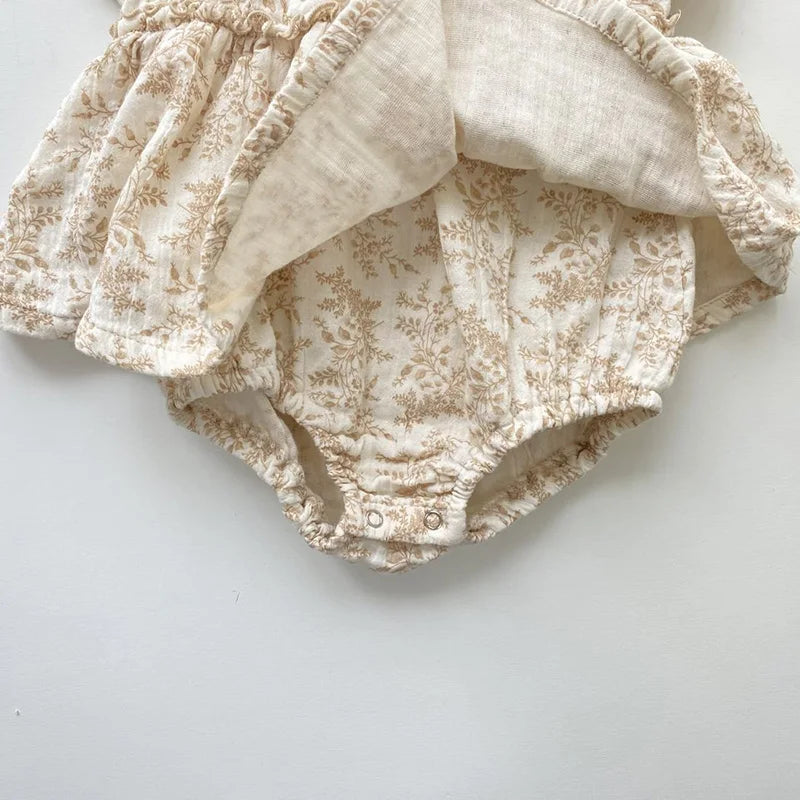 Cream floral baby romper with ruffle skirt and snap closures for newborns