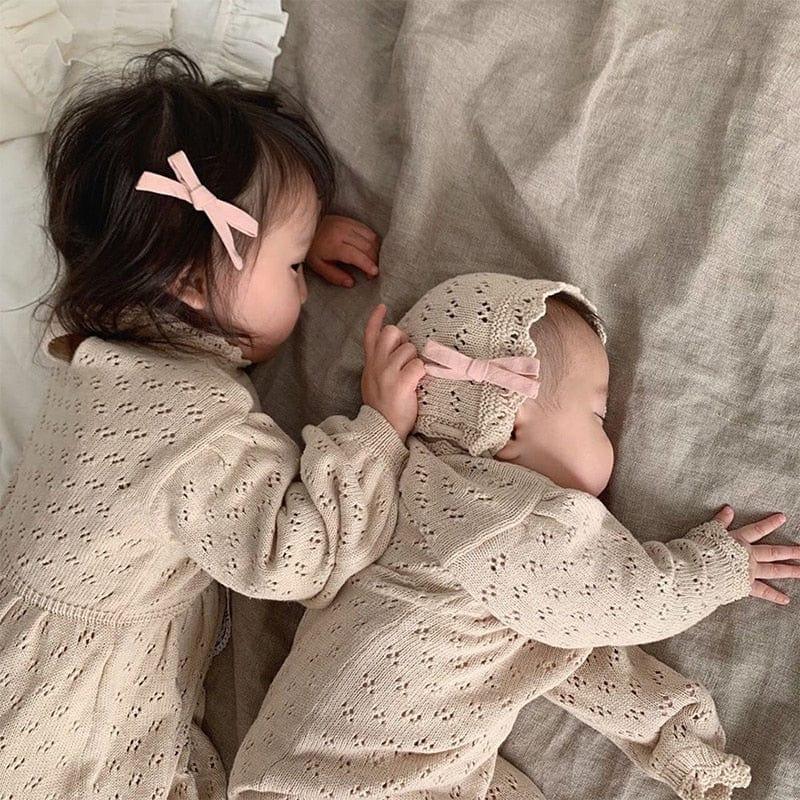 Beige knitted romper for babies with delicate eyelet pattern and matching bonnet with pink bow