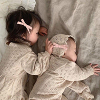 Beige knitted romper for babies with delicate eyelet pattern and matching bonnet with pink bow