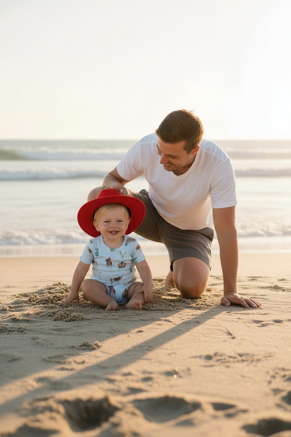 baby boys light blue shorty romper with animal print and red sun hat on beach