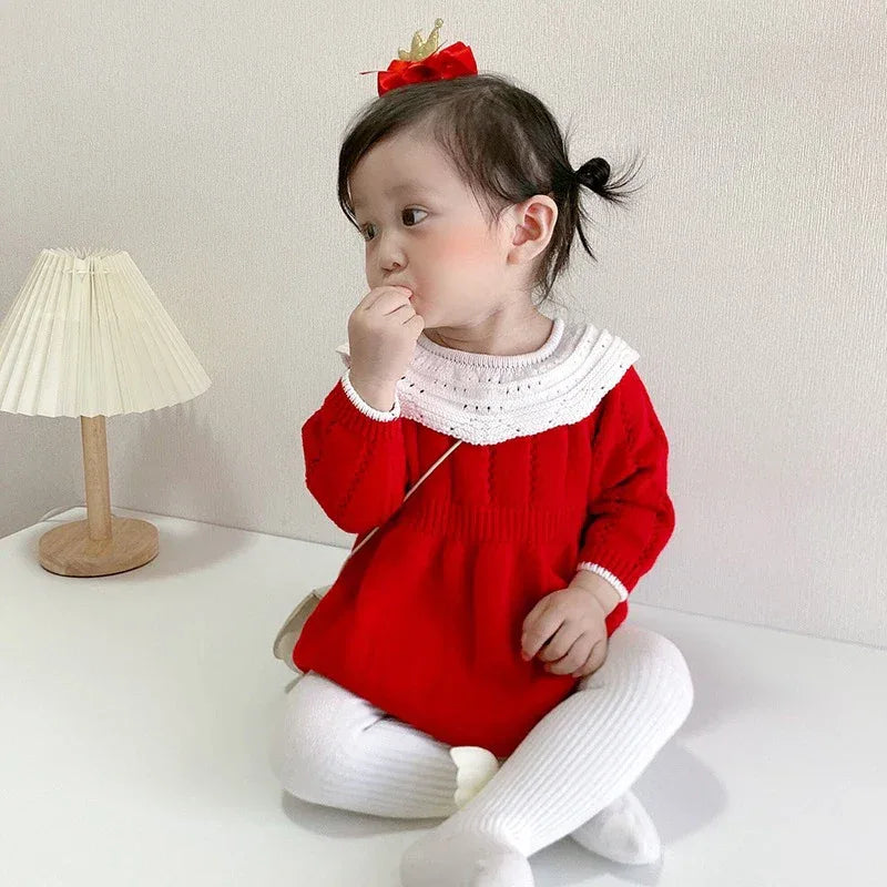 Baby girl red romper with white knit collar and long sleeves, sitting with white tights and matching red hair bow