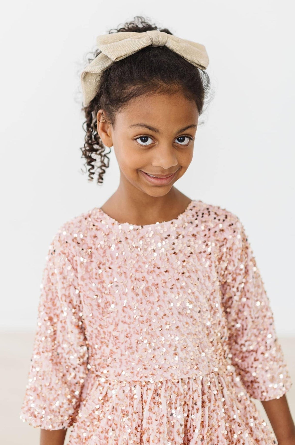 Girl wearing rose gold velvet sequin dress for girls smiling with beige headband