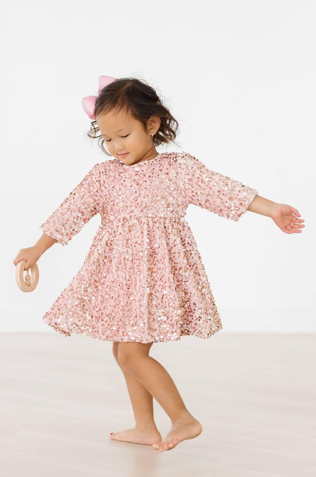 toddler girl wearing rose gold velvet sequin dress for girls twirling barefoot with pink bow in hair
