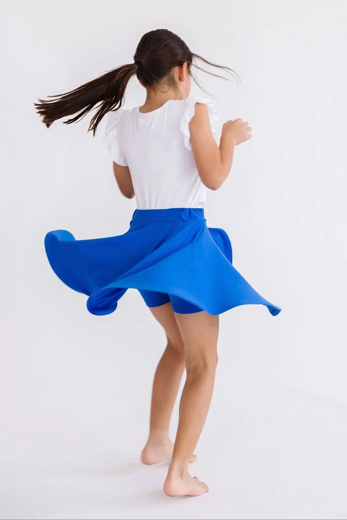 Girl wearing royal blue twirl skort for girls spinning with white top and ponytail